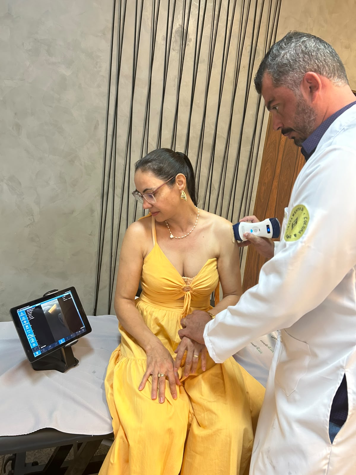 Dr. Luis Fêo realizando uma avaliação por ultrassom no ombro de uma paciente, no consultório